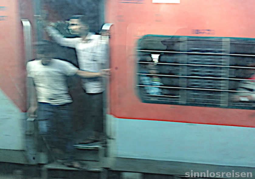 Männer halten sich an der Tür eines Zuges in Indien fest