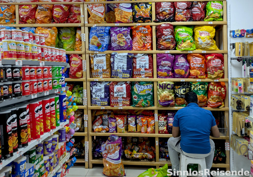 Mann sitzt vor Chipsregal im Supermarkt